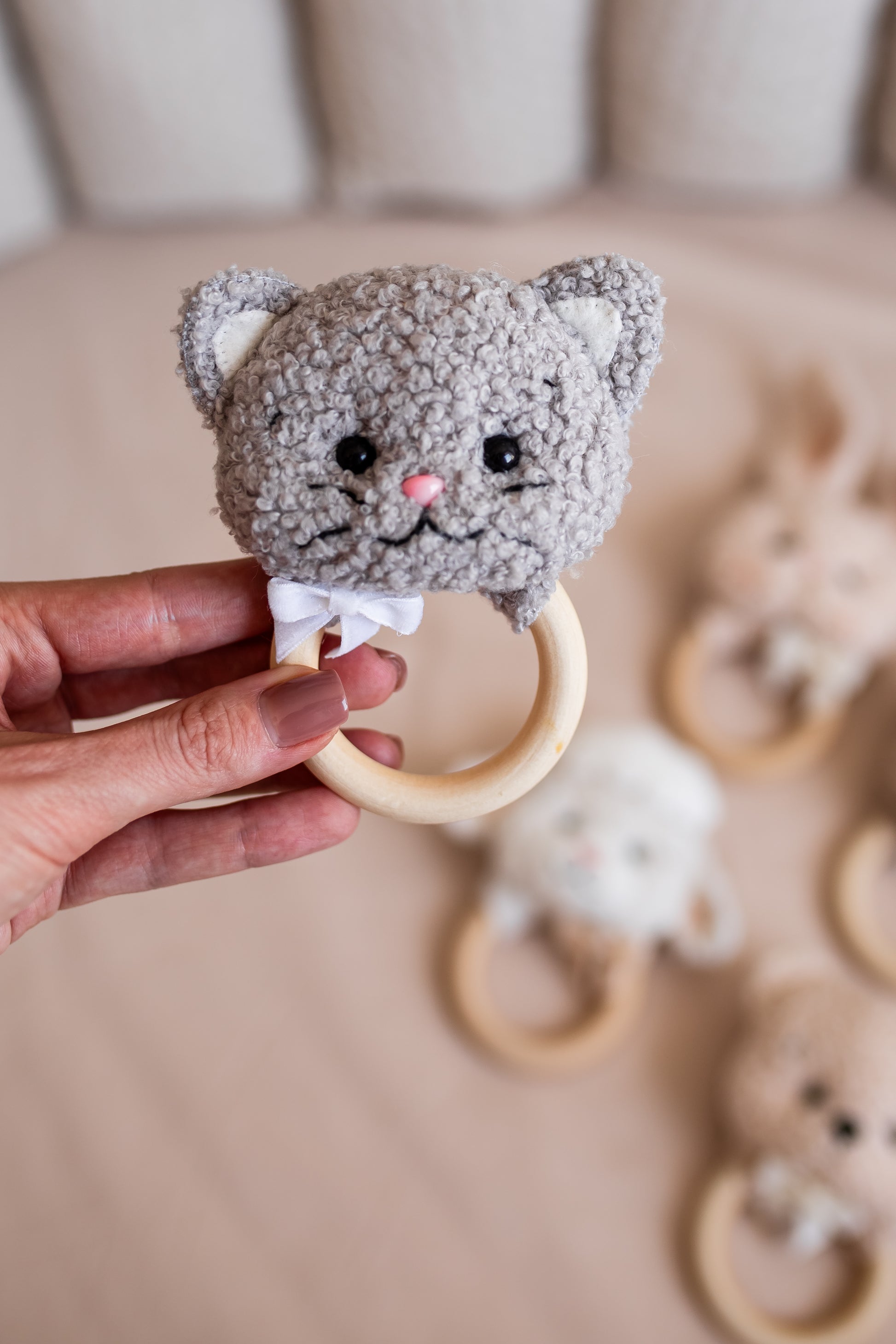 Hand holding a gray cat-shaped teething ring with a blurred background