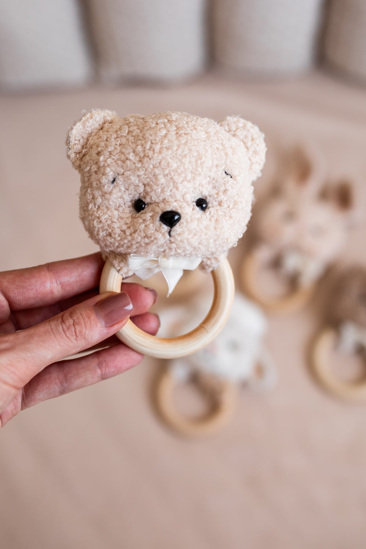 Hand holding a teddy bear-shaped wooden teething ring against a neutral background