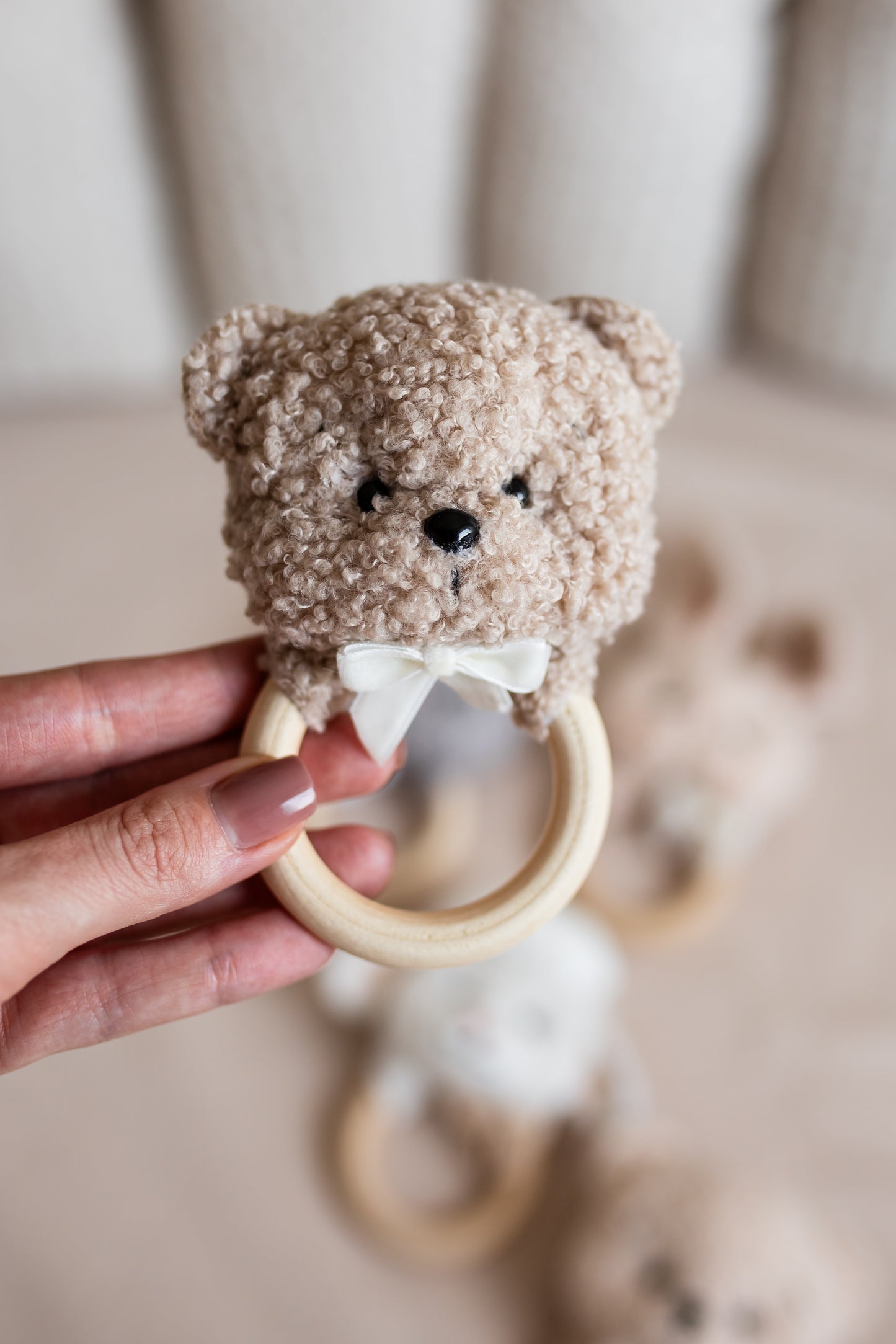 Teddy bear-shaped teething ring held by a hand against a blurred background