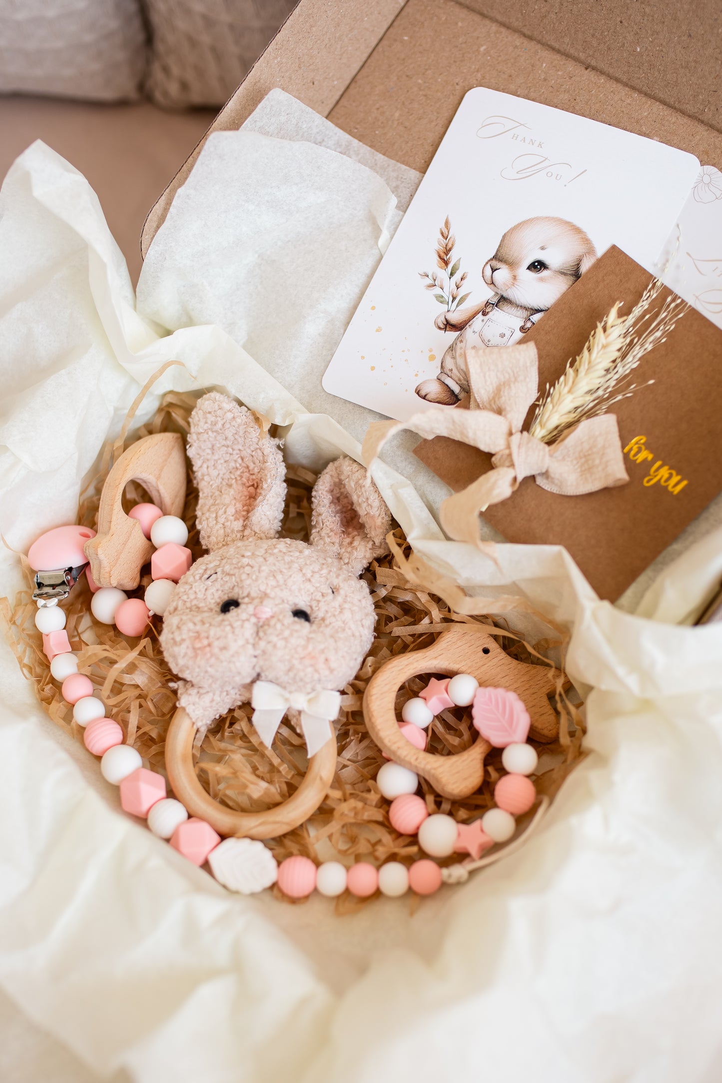 Baby teething ring with rabbit design and pink beads in a gift box with a card.
