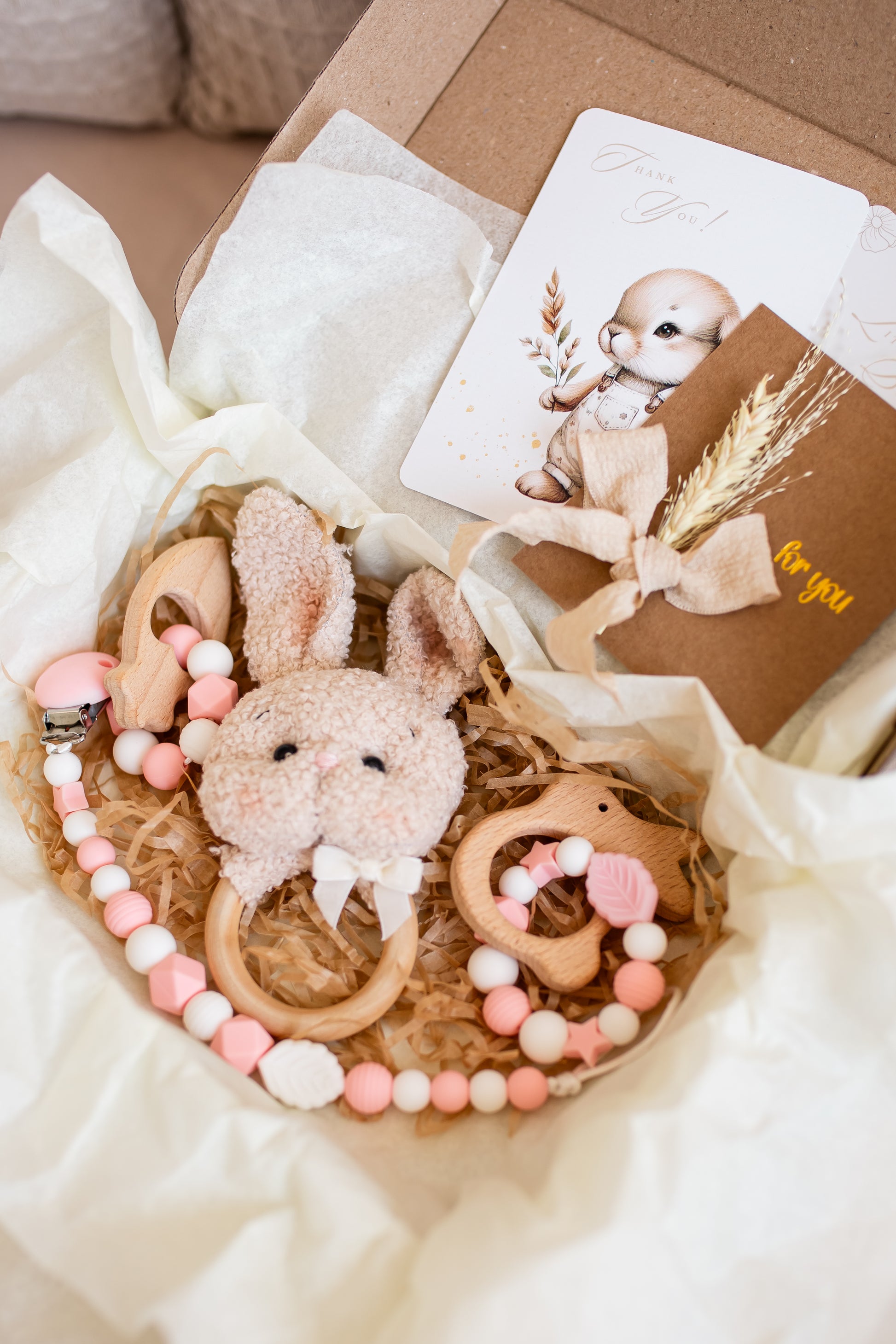 Baby teething ring with rabbit design and pink beads in a gift box with a card.
