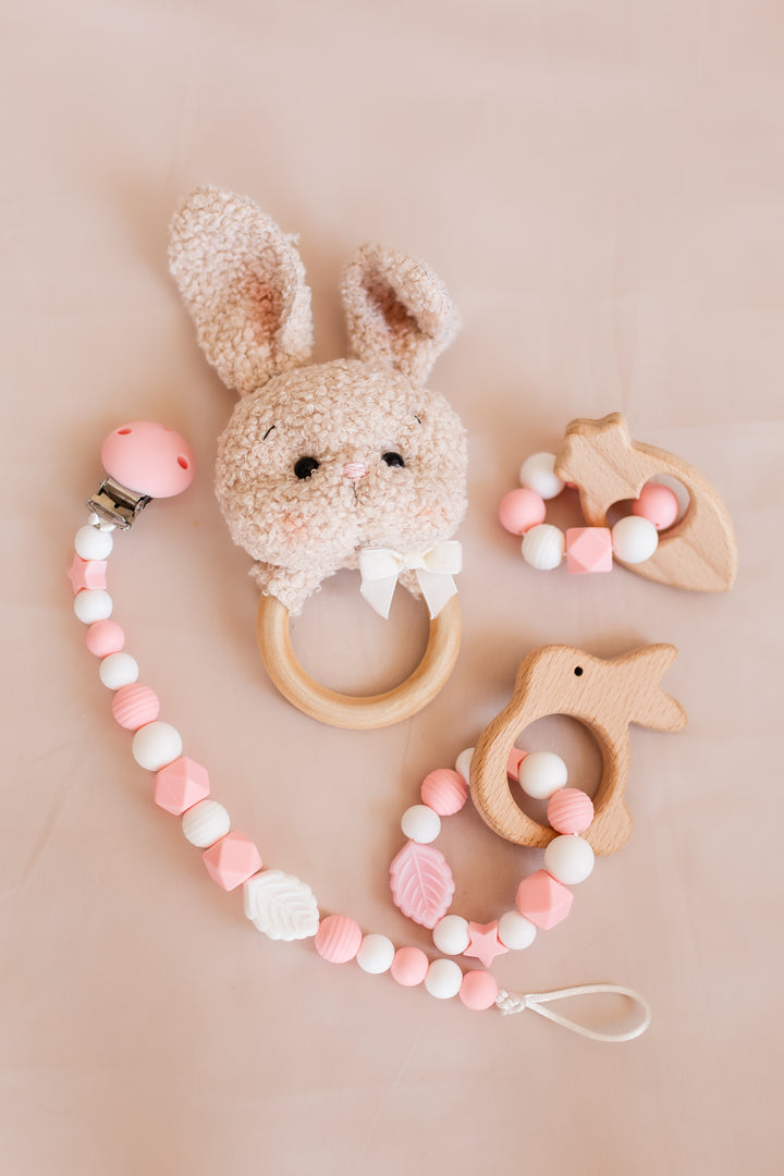 Baby teething toys including a bunny-shaped teether and a pacifier clip with beads on a beige background