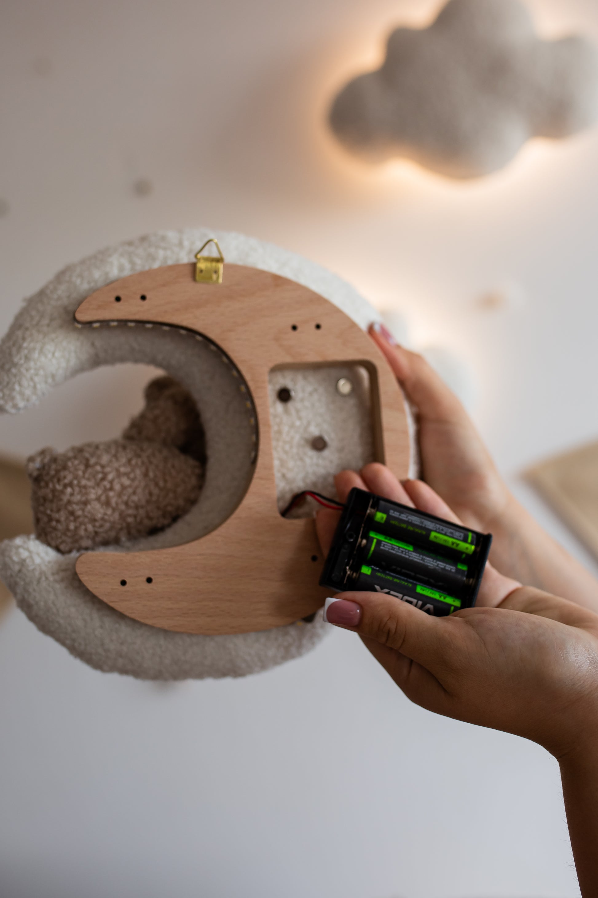 Wooden moon-shaped nursery night light with a fluffy texture, held by a hand with a smartphone.