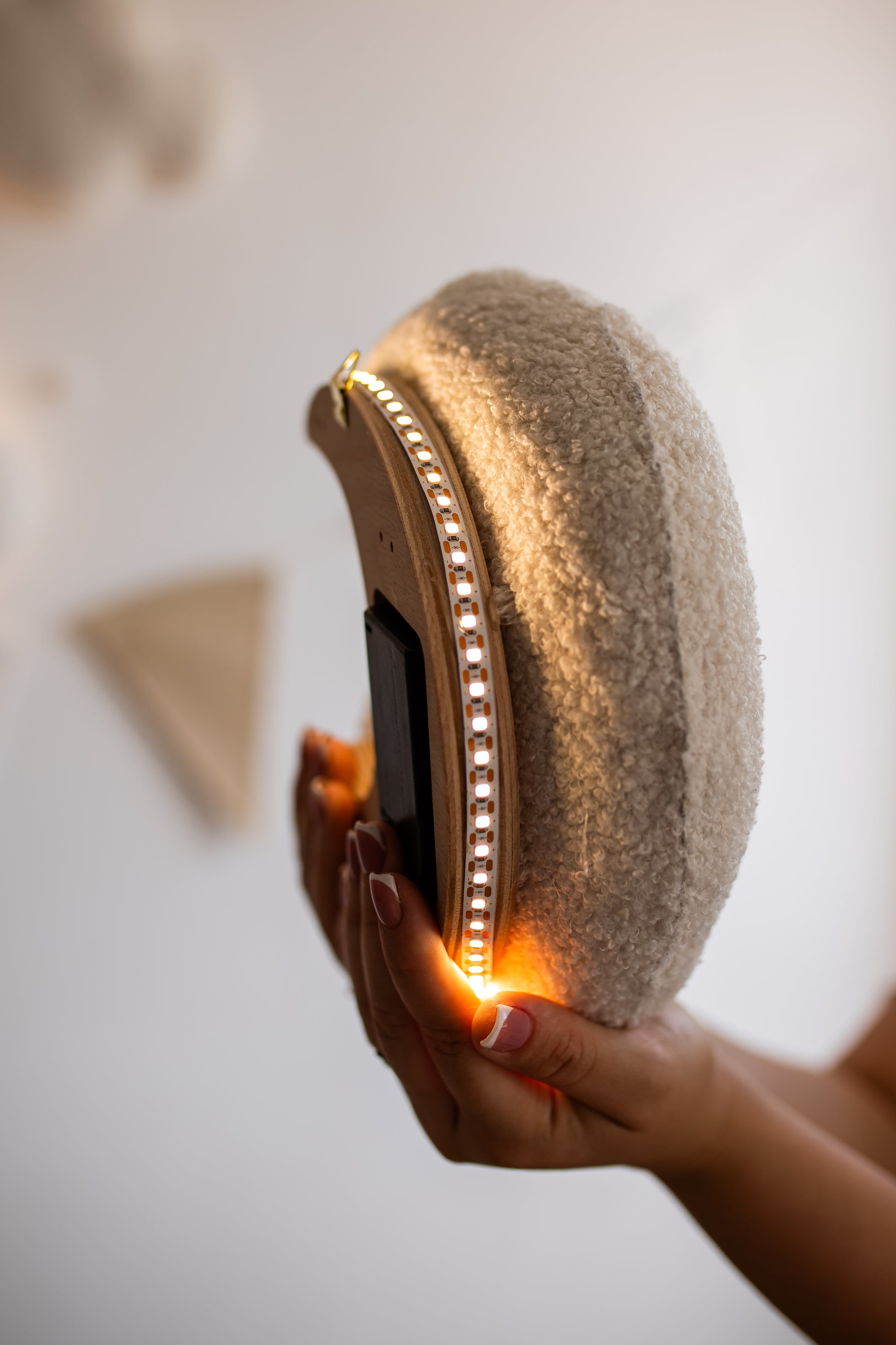 Hand holding a textured moon with a light inside against a neutral background