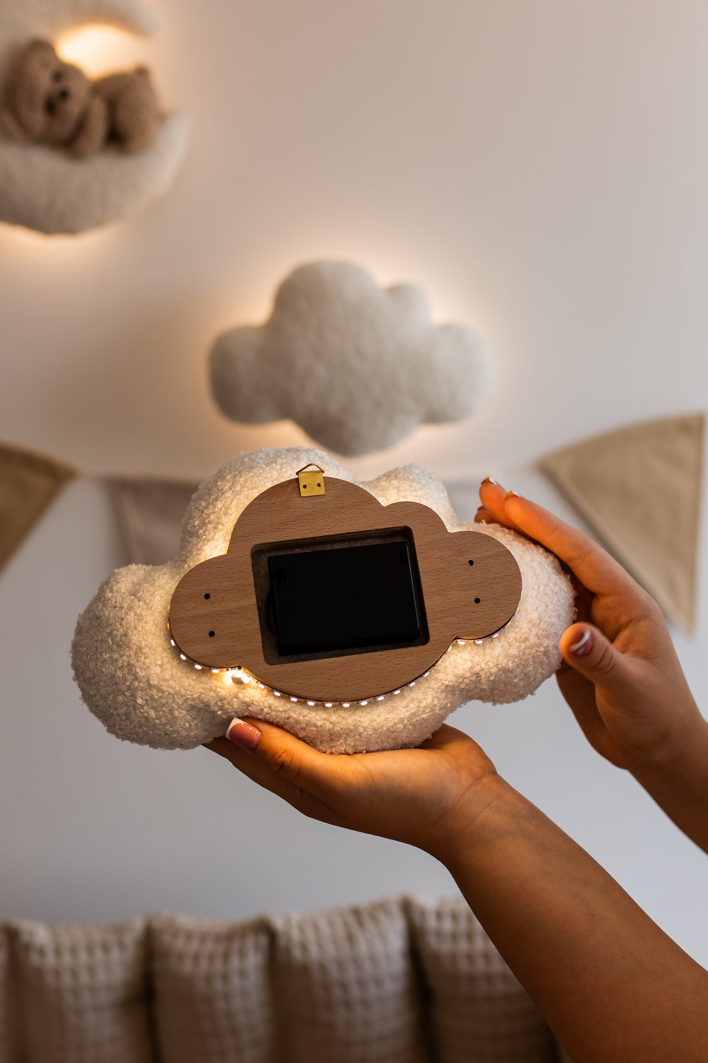 Person holding a cloud-shaped light element, surrounded by decorative pillows on a light-colored wall.