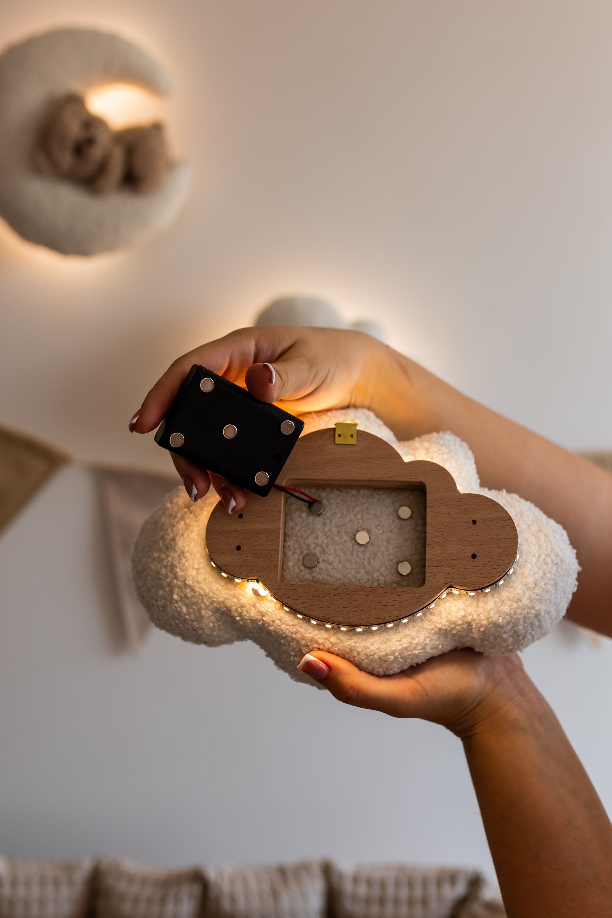 Hand holding a small boucle cloud light with LED lights inside, against a neutral background.