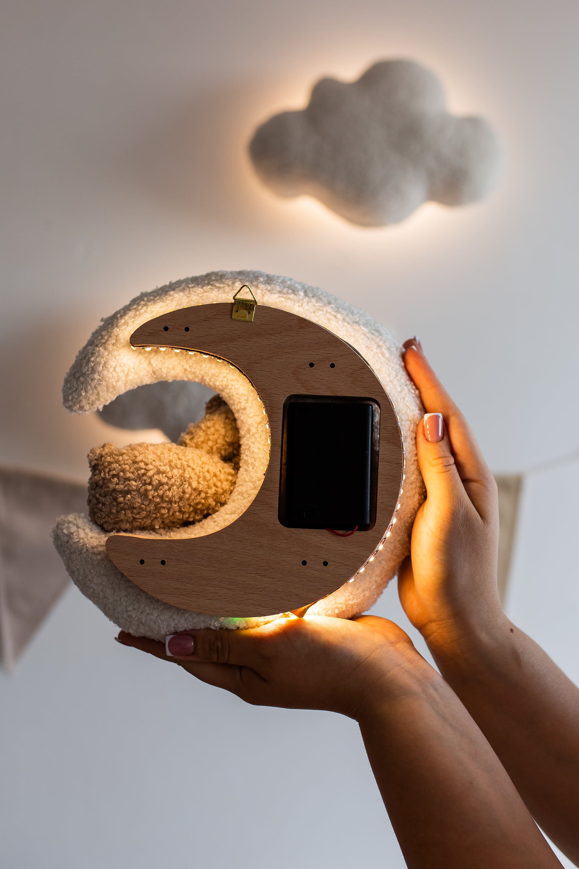Person holding a cloud-shaped night light with a small plush toy inside, against a neutral background.