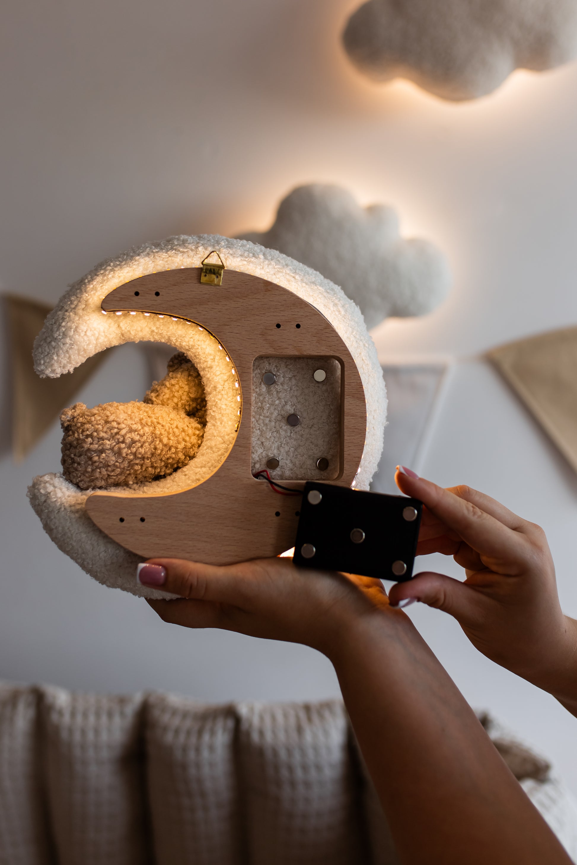 Person holding a wooden moon-shaped night light with a small animal inside, against a soft, blurred background.